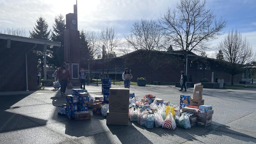 Donated food items laid out in front of the school. Students are carrying the items to the pile.