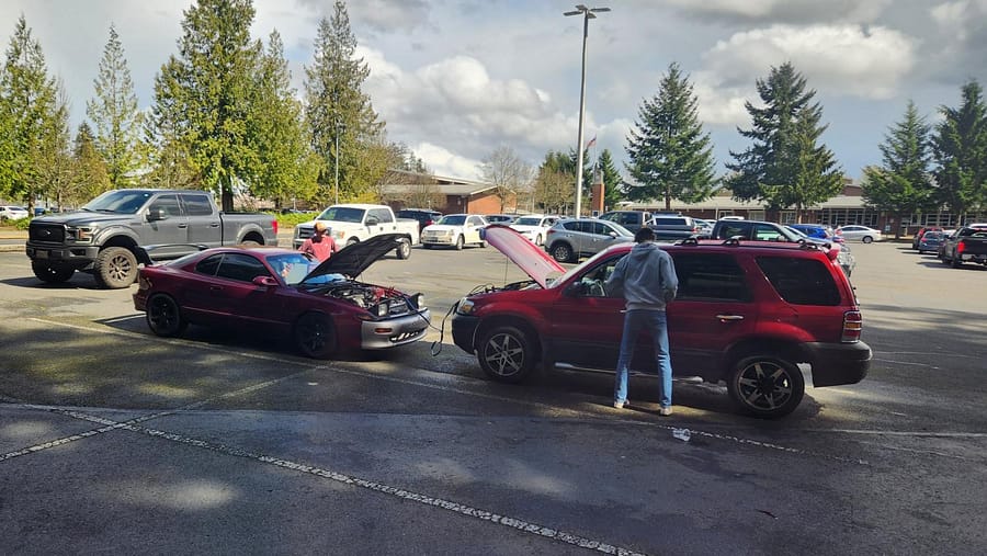 Two cars have their hoods up as they use jumper cables to give power to a car